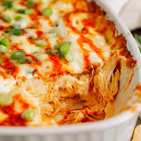 A hot, creamy bowl of Buffalo Chicken Dip with celery sticks and tortilla chips for dipping.