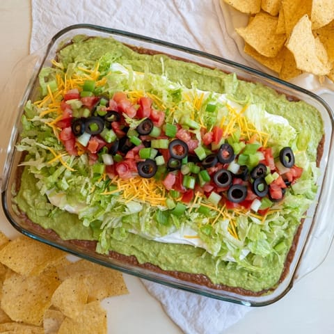 Classic Seven-Layer Dip featuring refried beans, sour cream, and fresh toppings like lettuce, green onions, and tomato in a chilled appetizer presentation.
