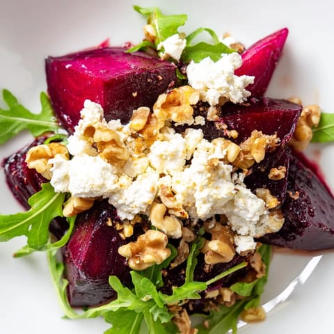 The Roasted Beet Goat Cheese Salad glistens with balsamic vinaigrette, featuring earthy beets, tangy cheese, and crunchy walnuts on a bed of greens.  