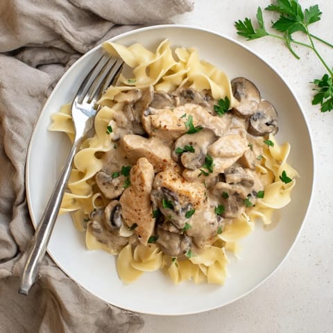 A hearty serving of Chicken and Mushroom Stroganoff features golden chicken, earthy mushrooms, and a rich, velvety sauce atop a bed of noodles.  