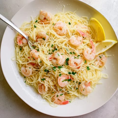 A close-up view of Lemon Butter Shrimp Pasta Lite garnished with fresh parsley and served with lemon wedges.