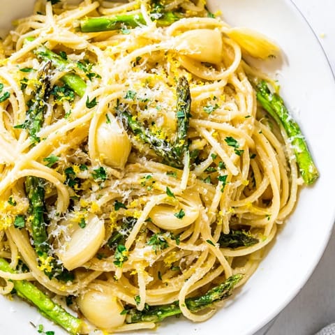 A close-up of bright green asparagus and mashed roasted garlic tossed with spaghetti for an easy spring dinner. 
