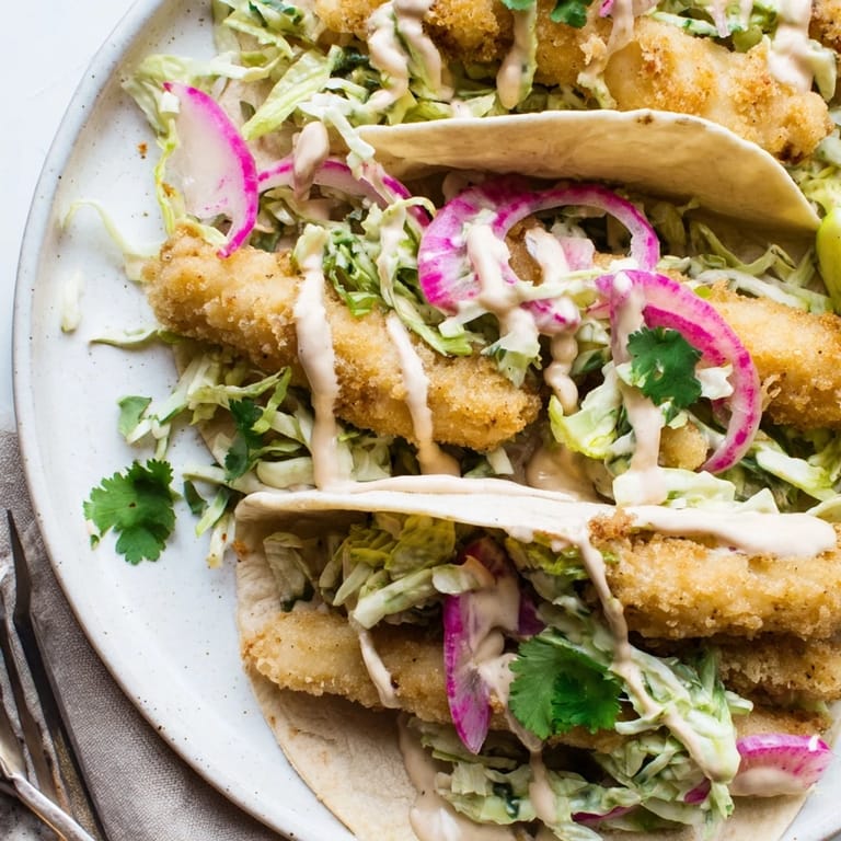 Crisp Baja Fish Tacos filled with white fish, cilantro, and red onion, drizzled with zesty lime crema.