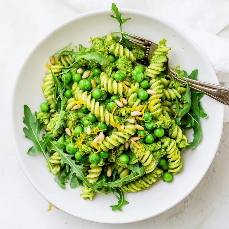 Close-up of Spring Green Pesto Pasta Salad, highlighting toasted pine nuts and crumbled feta over chilled pasta for a refreshing bite.  