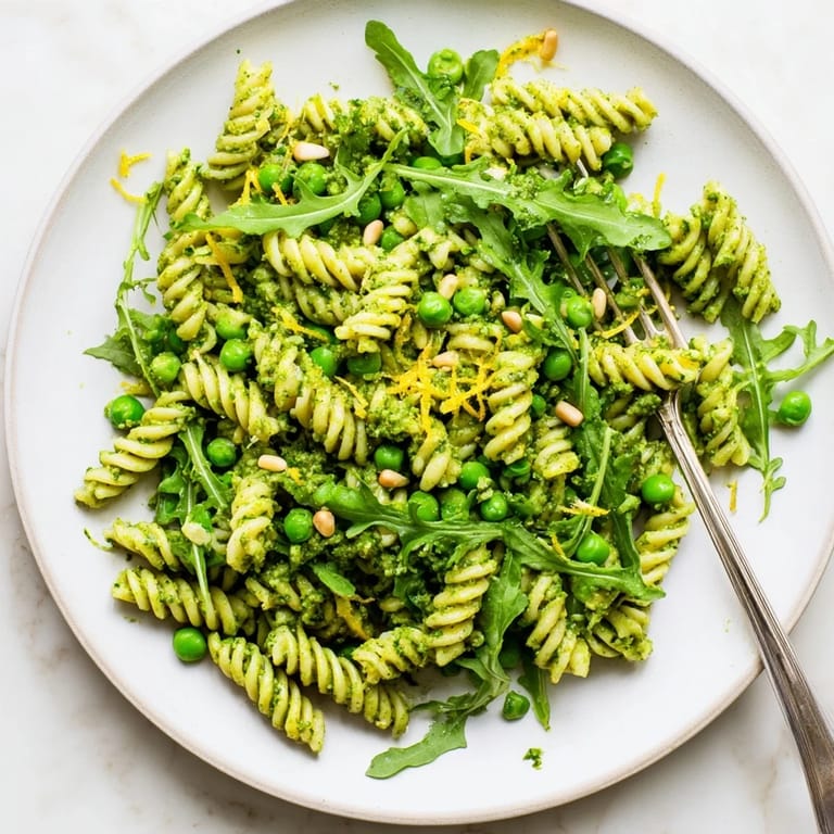 Spring Green Pesto Pasta Salad served in a white bowl, garnished with lemon zest and fresh herbs, perfect for a sunny picnic.