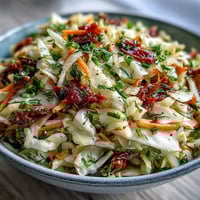 A vibrant bowl of Cabbage Salad With Sundried Tomatoes, tossed with crisp purple and green cabbage and sweet, chewy tomato pieces.